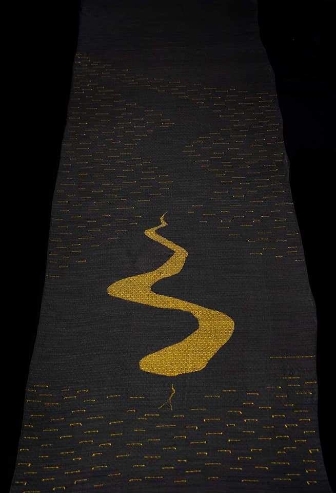 a black silk woven piece with a yellow clasp woven snake slithering through tsumugi silk inlays