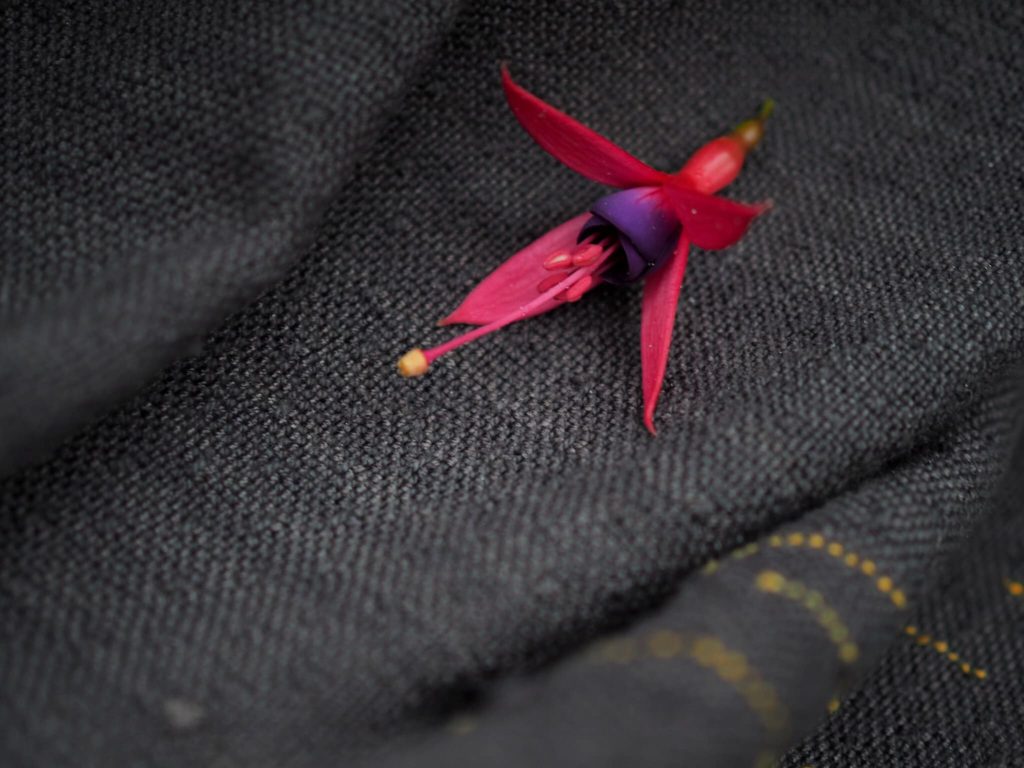 a fuchsia flower sits on the black silk weft