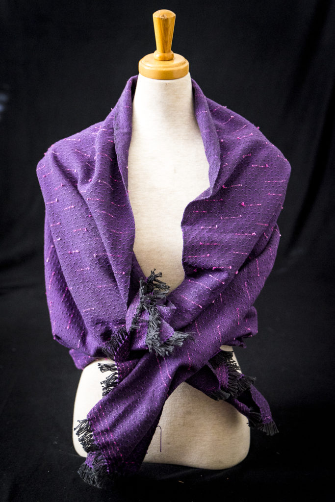a purple and black textured handwoven shawl sits on a model