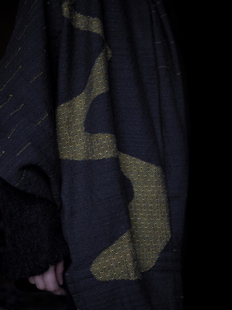 a black ring sling with a yellow snake in clasped weft is shown hanging from a shoulder
